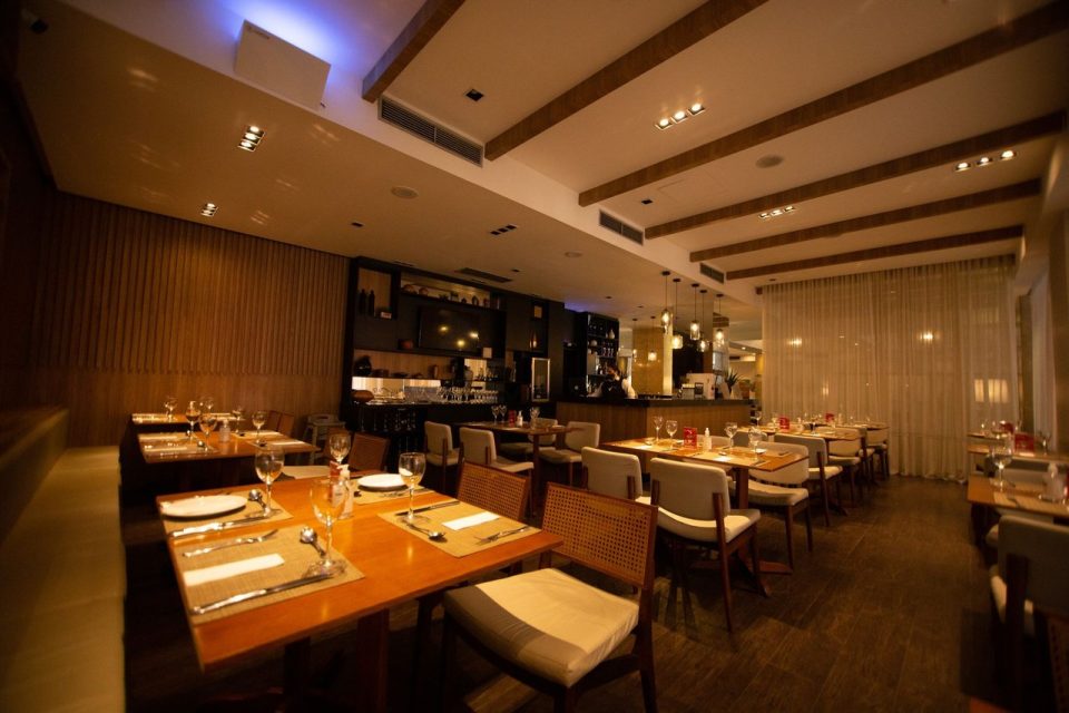 Interior de restaurante contemporâneo, com mesas postas e iluminação acolhedora, preparado para receber clientes.