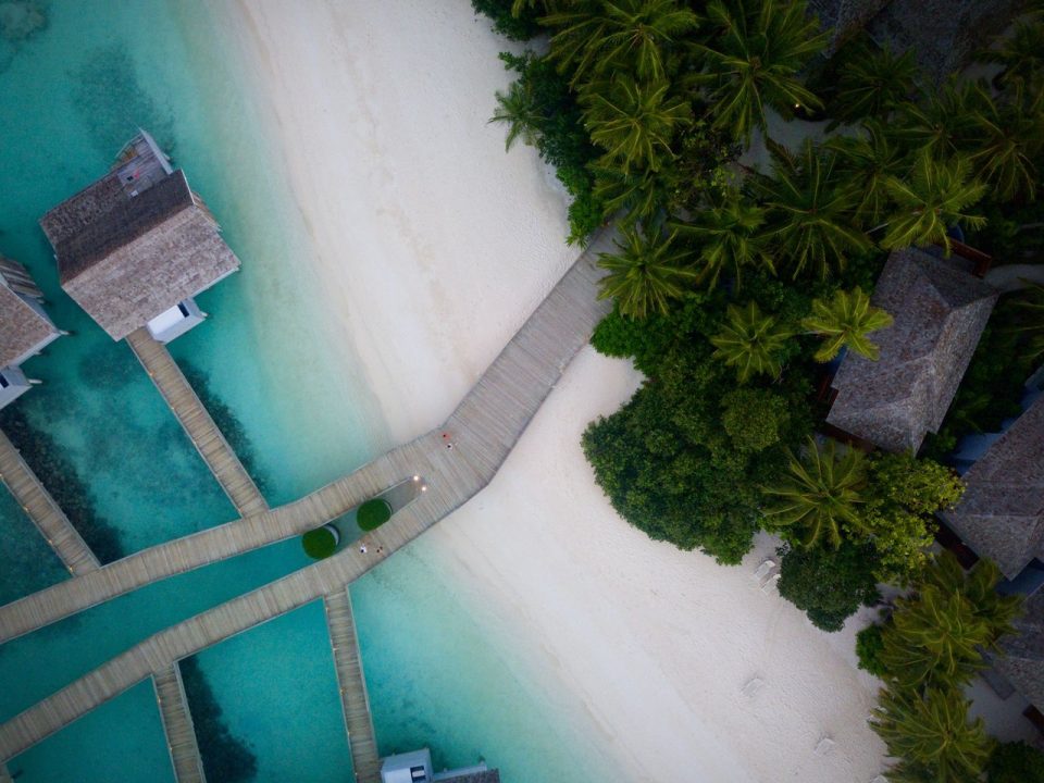 Vista aérea de um resort tropical à beira-mar, cercado por vegetação e águas azul-turquesa.