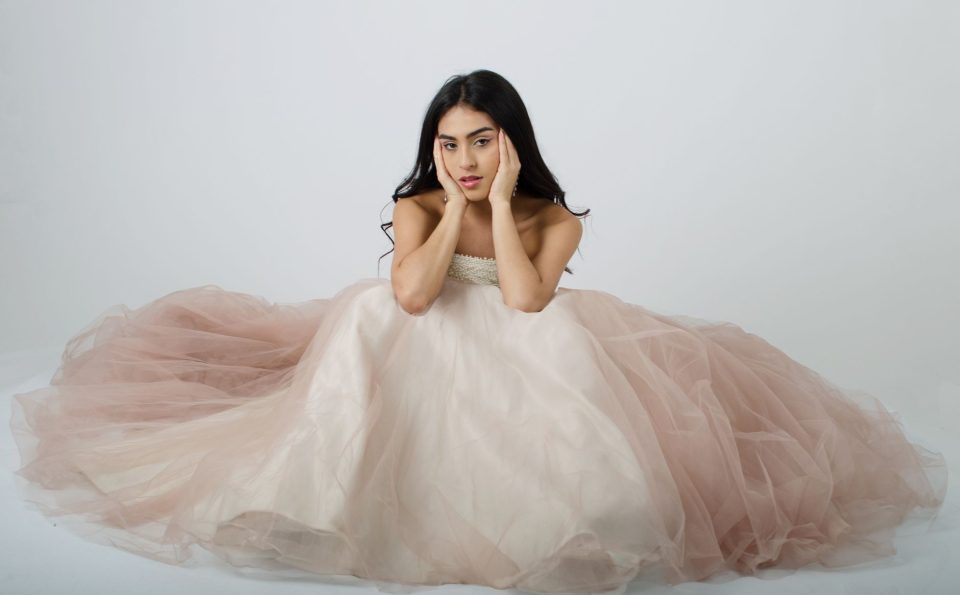 Mulher posa em estúdio usando um elegante vestido longo em tom pastel, com fundo neutro.